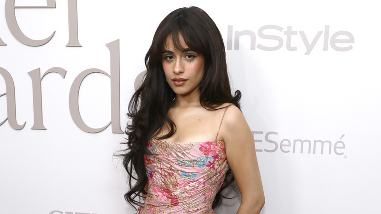 Camila Cabello posing on step-and-repeat in pink floral dress with long hair cascading over her right shoulder