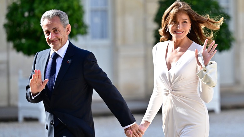 Nicolas Sarkozy and Carla Bruni-Sarkozy waving to the camera as they walk hand-in-hand