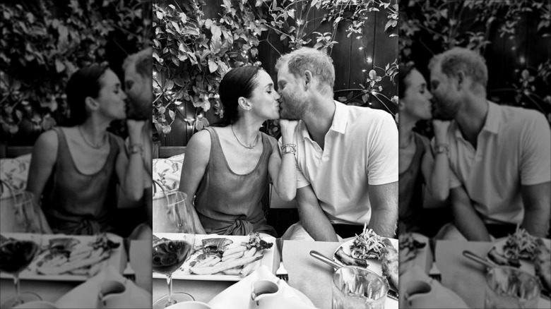 Black and white photo of Meghan Markle and Prince Harry kissing over dinner