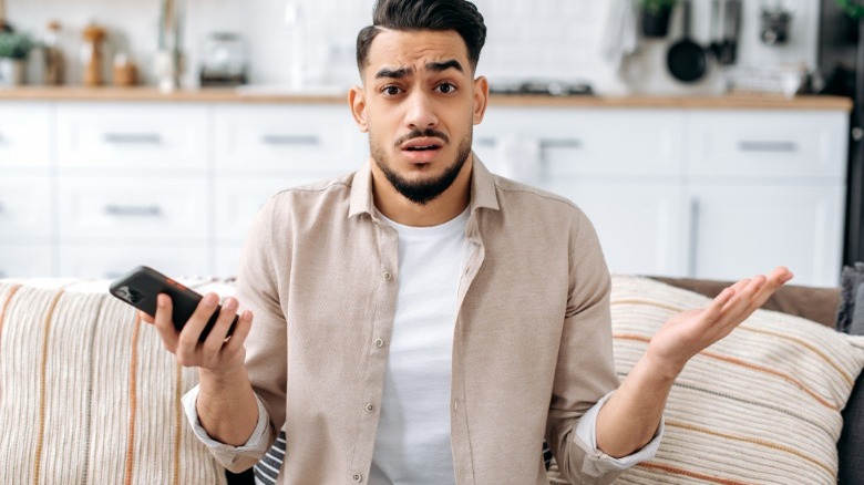 Confused man shrugging holding phone