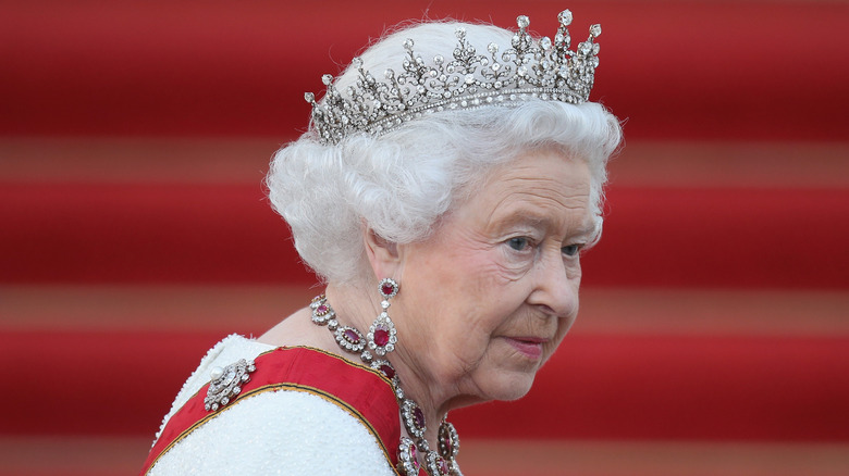 Queen Elizabeth II wearing tiara against red backdrop