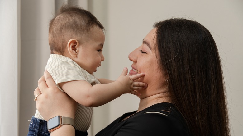 Woman holding up baby who is touching her face