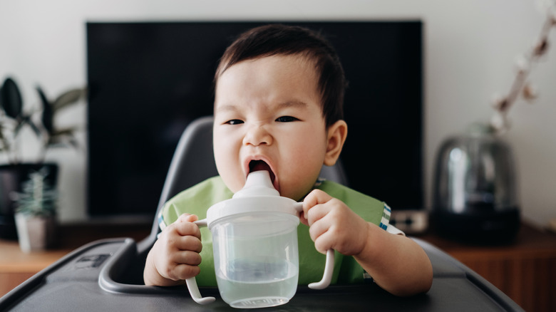 Baby drinking water from a cup in a high chair