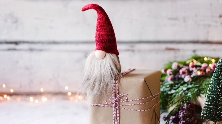 The cutest tiniest gnome covered in beard hair with a tall red hat sits on a Christmas present