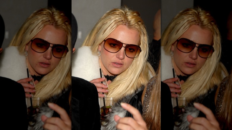 Closeup of Britney Spears walking through crowd wearing sunglasses and holding a drink with straw