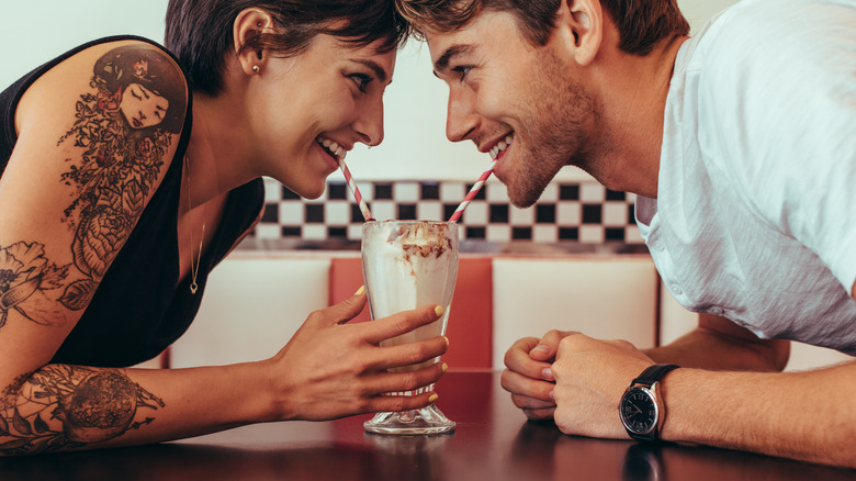 man and woman sharing milkshake