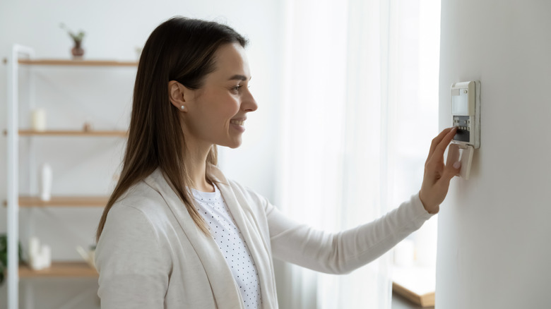 Woman adjusting the thermostat inside house