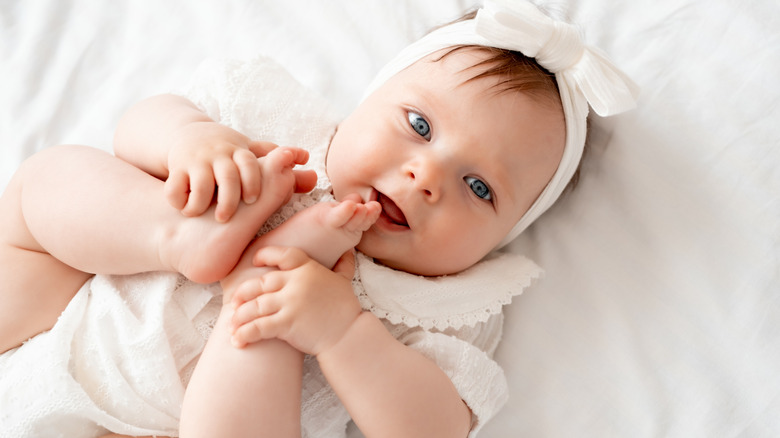 Baby with bow putting toes in her mouth