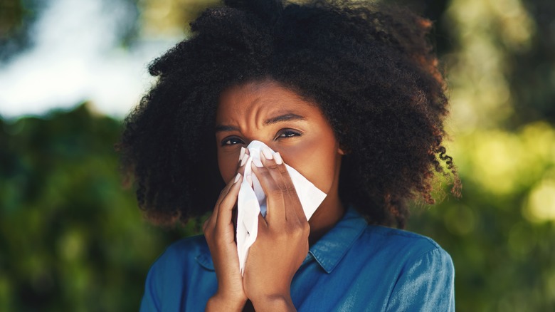 Woman blowing nose in tissue outdoors