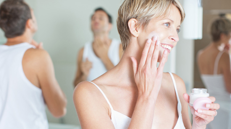 woman moisturizes while man ponders