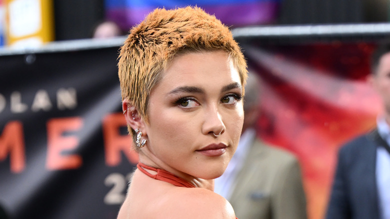 Florence Pugh looking over her shoulder posing with orange pixie cut