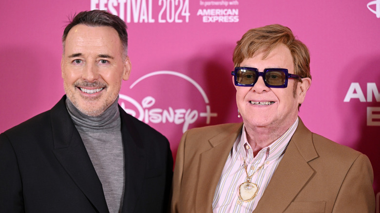 Elton John and David Furnish posing against pink background