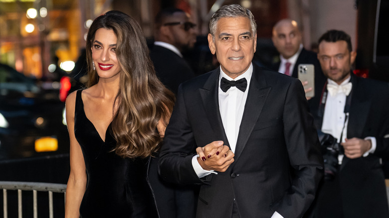 George Clooney and Amal Clooney holding hands in black formals