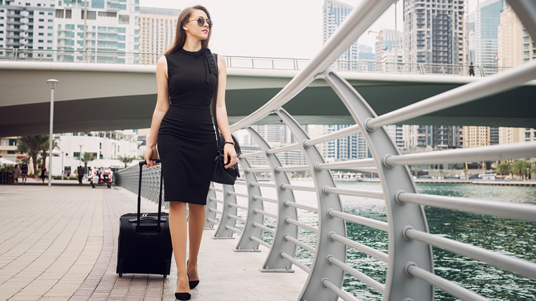 Woman in black dress wheels suitcase 