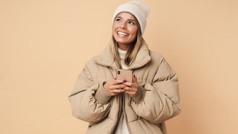 Woman wearing coat and hat smiling holding phone