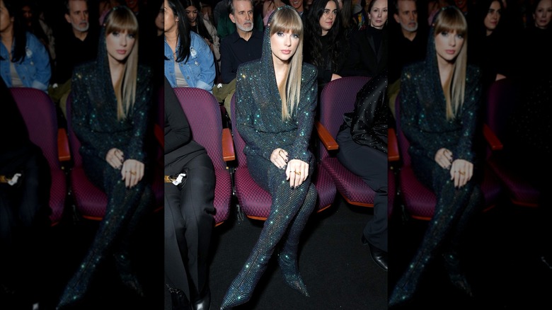 Taylor Swift sits in a hooded, bedazzled bodysuit 