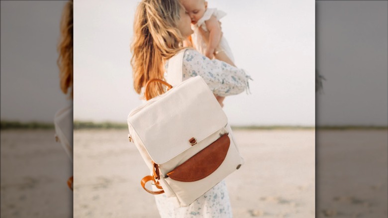 woman on beach with backpack holding baby