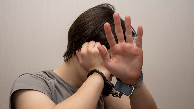 Handcuffed teen hiding face