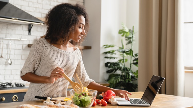 Woman cooking while using a laptop