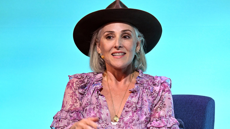 Ricki Lake speaking on stage in a hat and pink floral dress