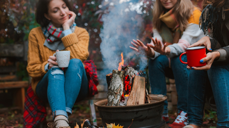 Women in sweaters sitting around a fire with mugs