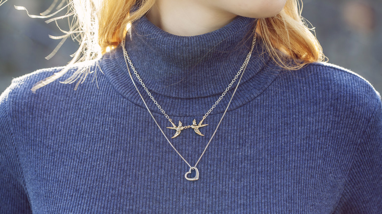 Woman wears blue turtleneck and two chain necklaces