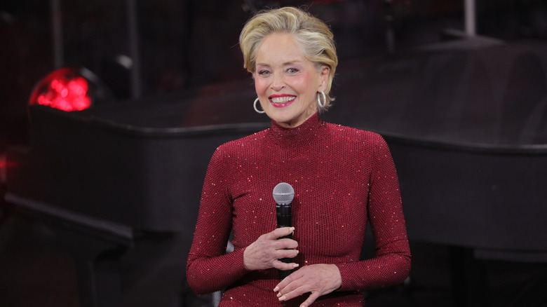 Sharon Stone wears a red dress and holds a microphone