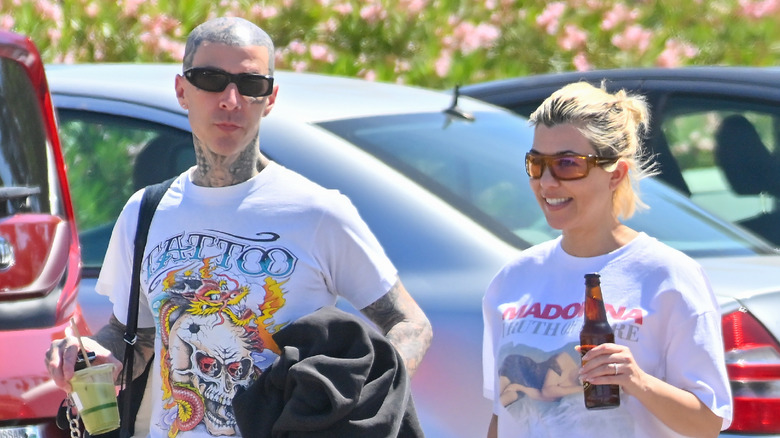 Travis Barker and Kourtney Kardashian wear casual clothing and sunglasses, while on a walk