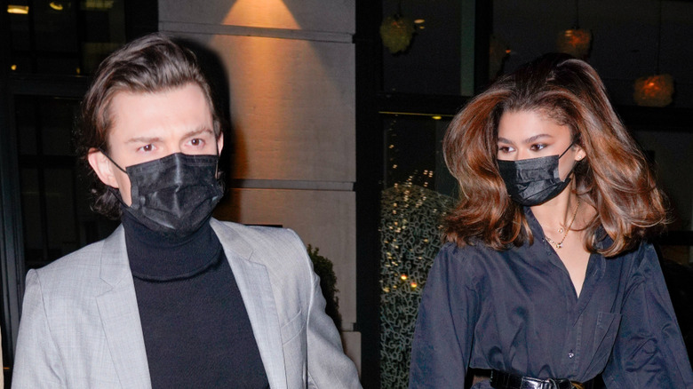 Tom Holland and Zendaya walking hand in hand and wearing face masks