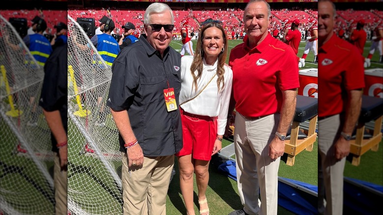 Sarah Huckabee Sanders standing on a football field with two other people; she's wearing red leather shorts and a white blouse.