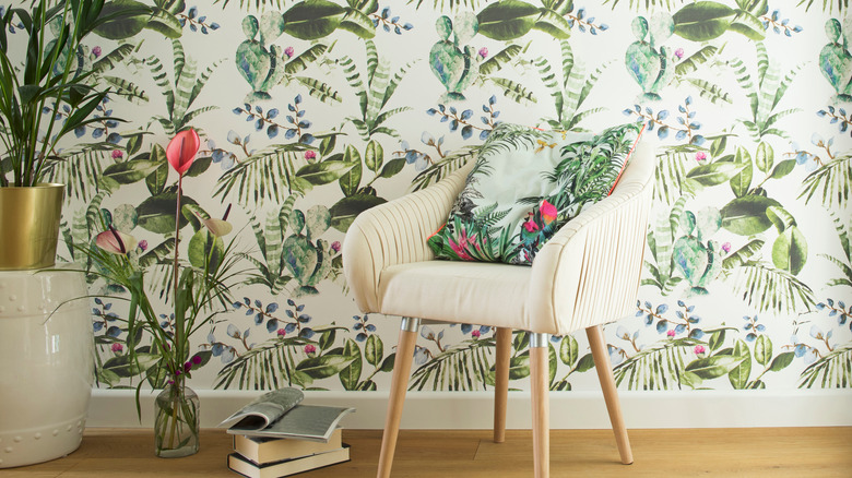 Cream chair sitting on a wooden floor in front of floral wallpapered wall.