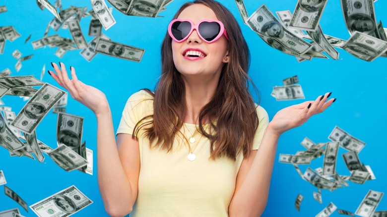 Woman with heart-shaped sunglasses looking up as $100 bills fly around her