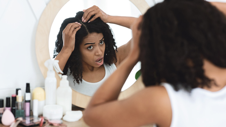 woman examining her scalp in the mirror