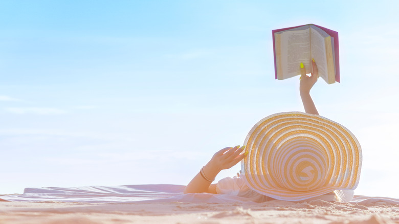 woman laying on the beach holding a book 