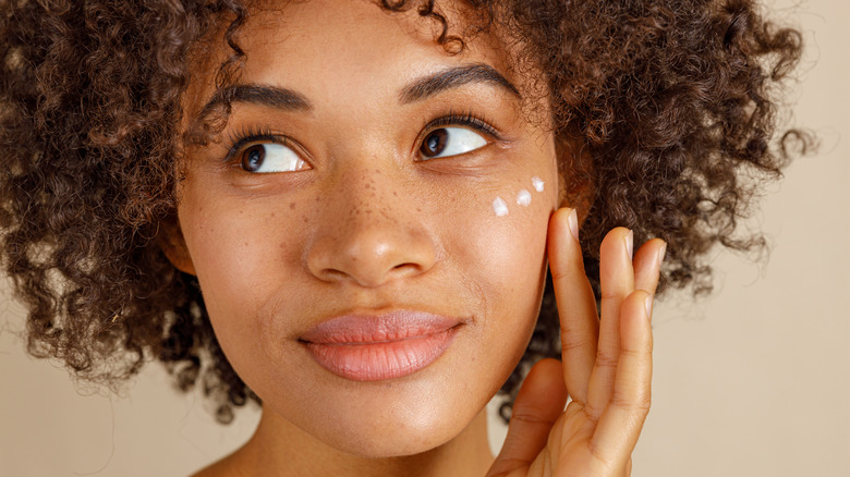 Woman smiling while applying moisturizer