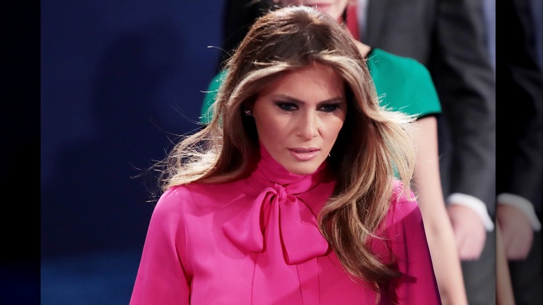 Melania Trump wearing a bright pink shirt with a big, fluffy bow at the neck.