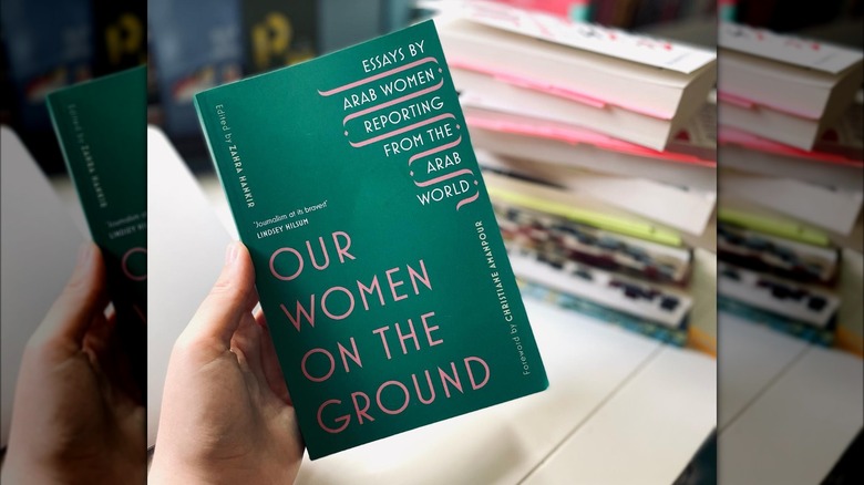 Hand holding "Our Women on the Ground" against other books