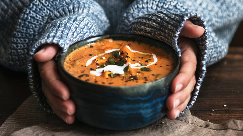 hands holding bowl of pumpkin soup