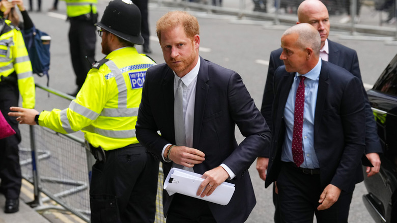 Prince harry on busy street carrying papers