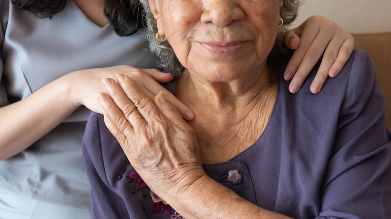 Layered hands of older and younger women on older woman's shoulder