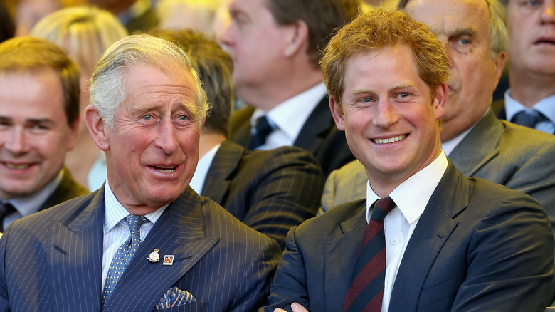 King Charles III and Prince Harry smile standing next to each other