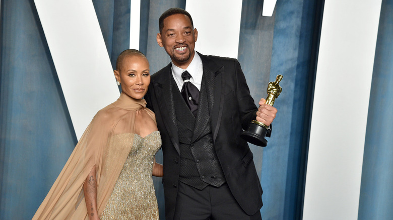 Jada Pinkett Smith looking serious while Will Smith smiles holding his Oscar award