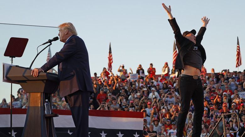 Elon Musk jumping while Donald Trump gives a speech