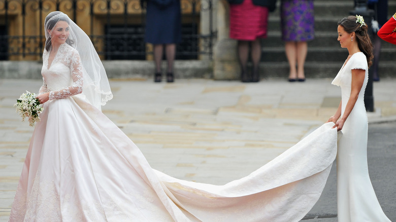 Catherine, Princess of Wales smiles in her wedding dress as Pippa Middleton holds her train