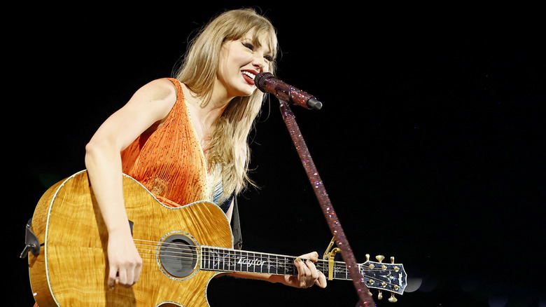 Taylor Swift smiling while playing the guitar at the Eras Tour