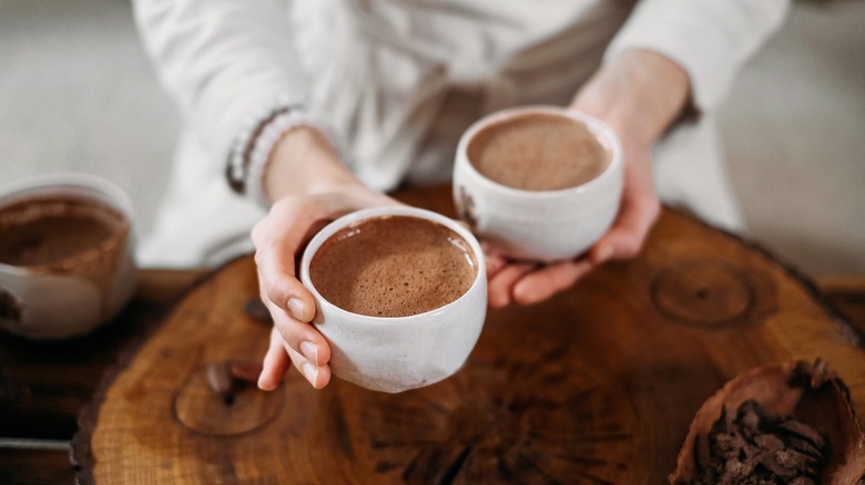 person holding two mugs of cocoa