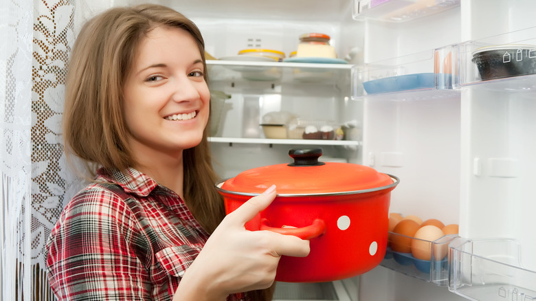 Woman puts dish in fridge