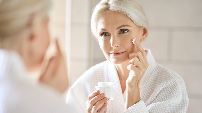 Woman applies face cream in the mirror