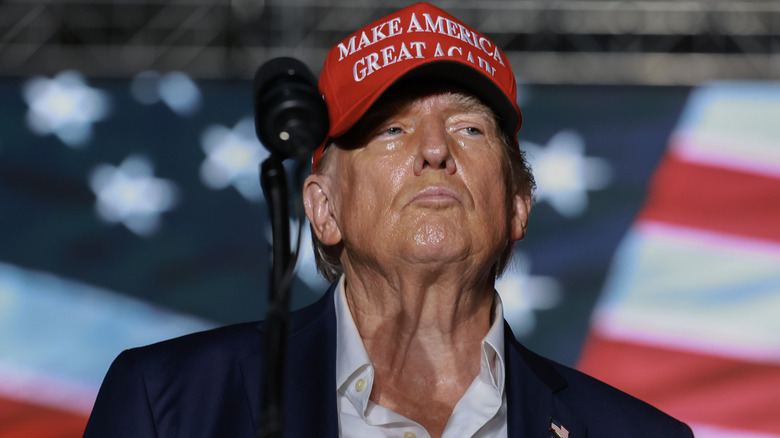 Donald Trump with an open collar, red Maga hat, and a shiny, sweaty, face.