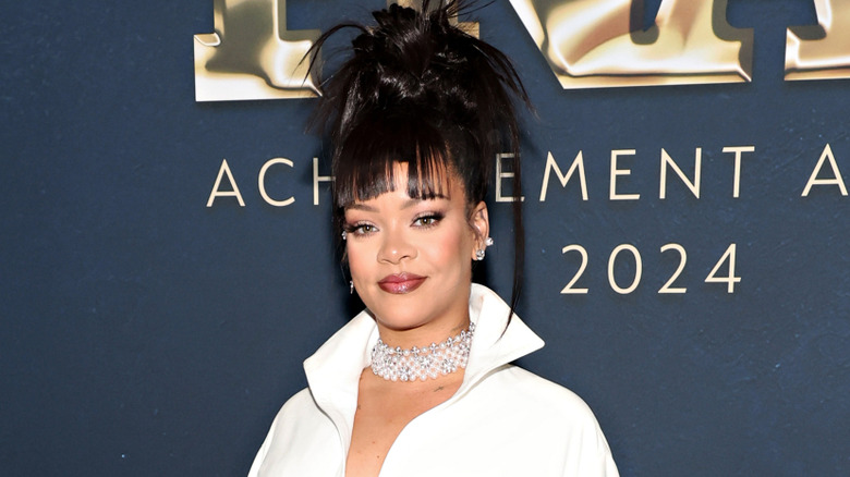 Rihanna wearing a white long-sleeved collared top and a chunky choker necklace, with a dark updo featuring blunt bangs